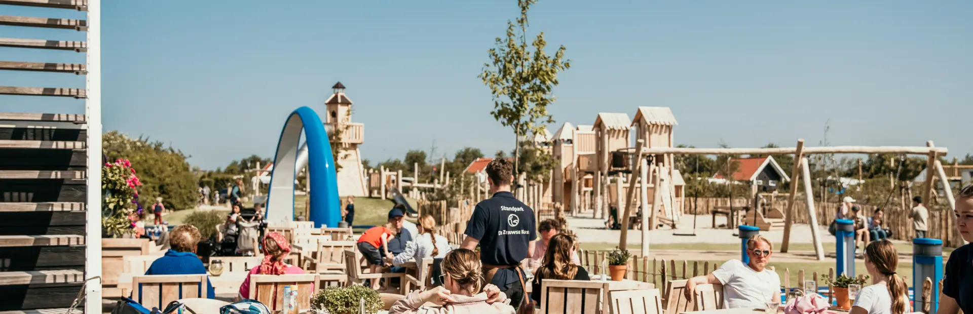 Gezellig terras bij De Zeeuwse Kust, ontspannen tafelen terwijl kinderen spelen op de avontuurlijke speelplaats